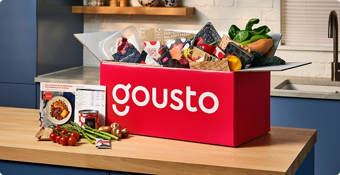 Open Gousto box showing fresh vegetables, fridge items in a chill box and recipe instruction cards