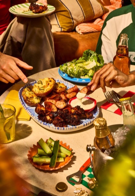 Hands reaching for roasted potatoes, sausages and dips on a shared platter, hosting friends at the table