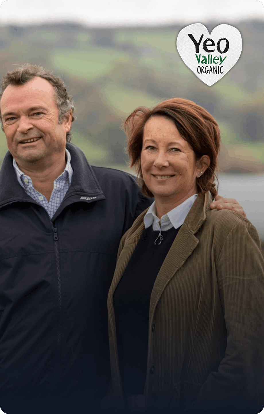 Smiling Yeo Valley owners standing in a green field with rolling countryside in the background