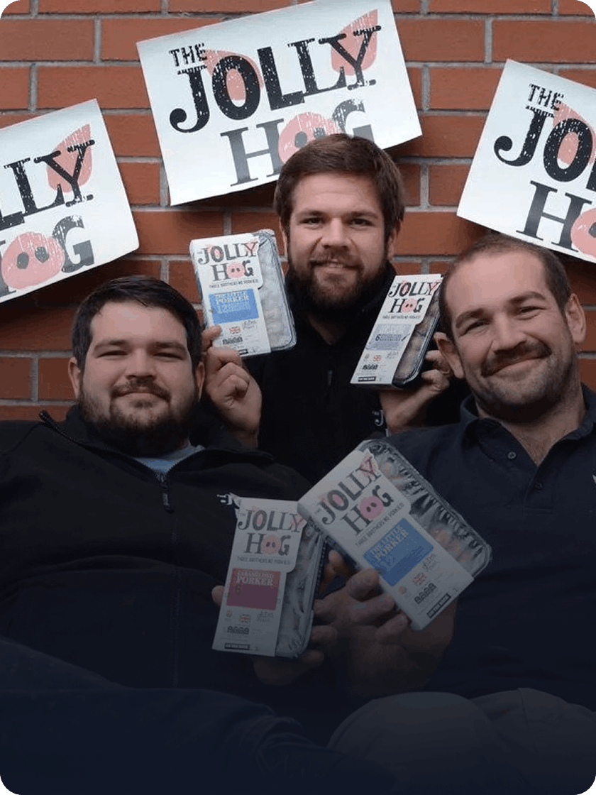 Three smiling The Jolly Hog owners holding packs of their sausages