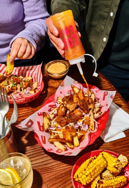 Hands dipping chips and fried chicken into sauces at a table, takeaway-style meal