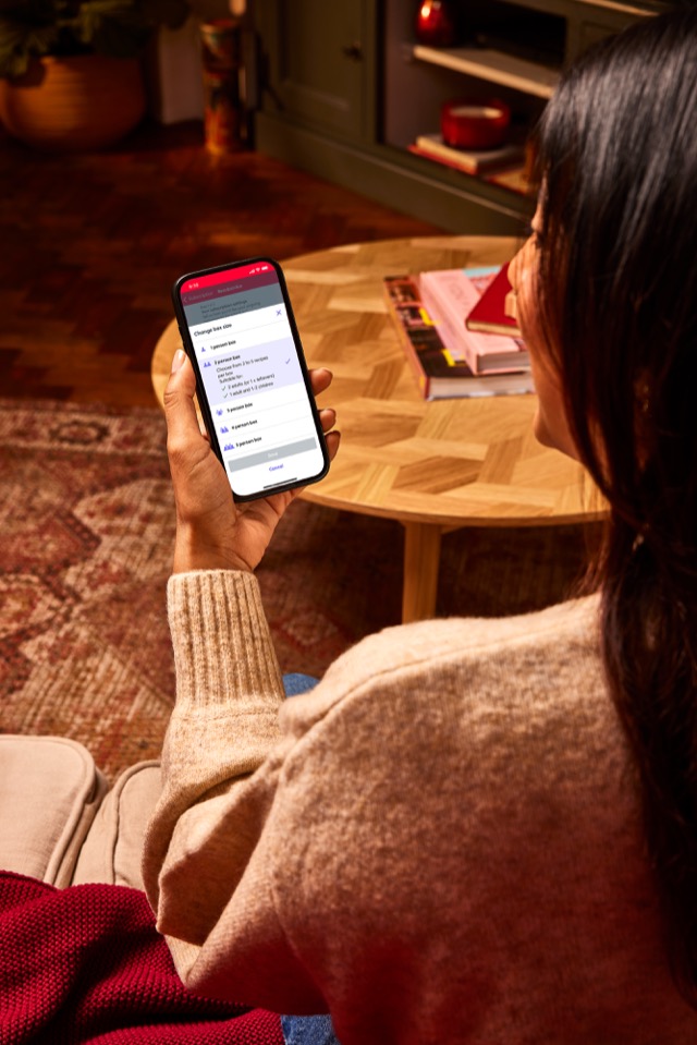 A woman using the Gousto app on a smartphone to change their box size and subscription settings