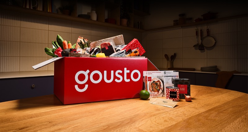 Open Gousto recipe box neatly packed with vegetables, meat, spices, and recipe cards.