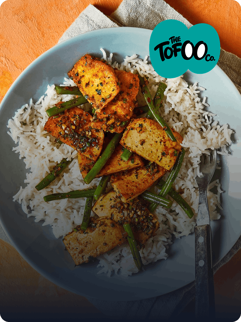 Spiced tofu and green bean stir-fry served over rice on a blue plate, with fork alongside
