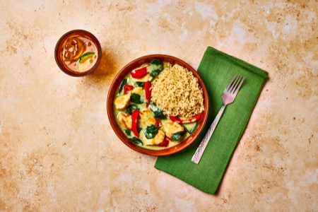 A bowl of green curry with chicken, veggies and brown rice