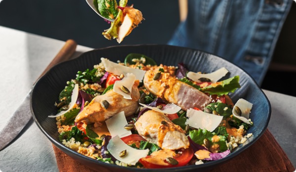 A big bowl of chicken salad with quinoa, vegetables, shaved cheese, herbs and seeds.